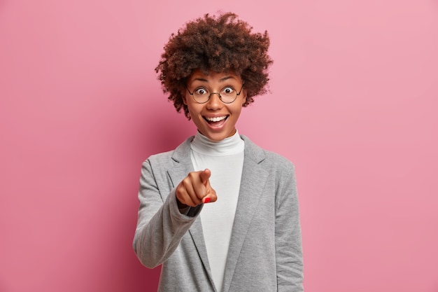 Glad dark skinned woman with Afro hair points index finger directly at you