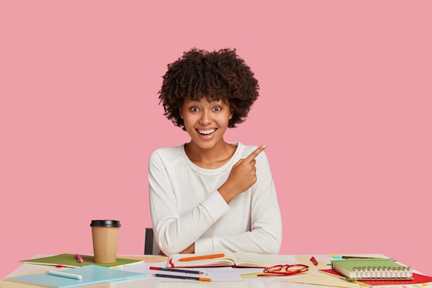 Glad female architect or designer draws sketch in notebook, sits at desktop with necessary things for work