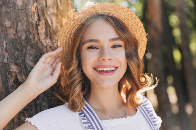 여름 날에 웃 고 모자에 다행 여성 모델. 숲에 웃 고 세련 된 곱슬 소녀의 야외 샷.