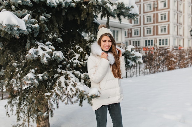 公園の散歩中に冬の日を楽しんでいる流行の服装でうれしい女性モデル。凍るような1月の日に路上で時間を過ごし、笑う笑う女性の屋外のポートレート。