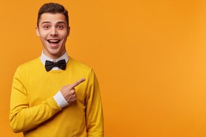 Glad happy man in yellow sweater over white shirt and black bow-tie pointing right with his finger