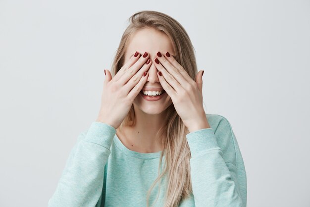 Glad happy young woman with blonde hair, closes eyes with hands