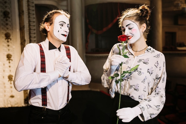 Free photo glad male mime artist looking at smiling female mime smelling red rose