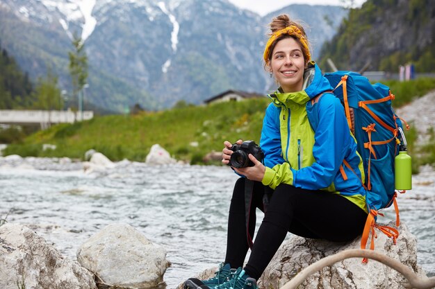 Glad optimistic female tourist rests outdoor on rock