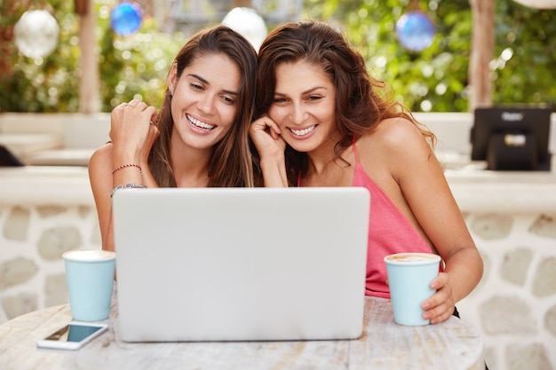 기쁜 예쁜 여성들은 커피 숍에서 자유 시간을 보내고, 노트북 컴퓨터에서 영화를 보거나, 화상 통화를하고, 무선 인터넷에 연결되어 있습니다.