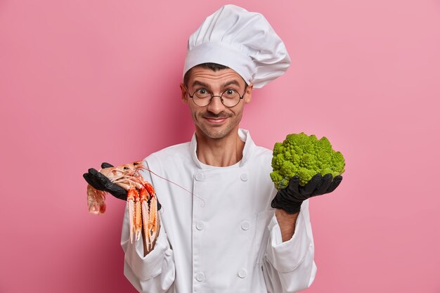 Felice chef professionista detiene crefish e broccoli crudi, felice di esporre qualcosa di nuovo nel cibo, cuochi in cucina