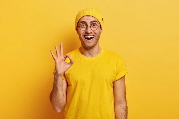 Glad satisfied man shows okay gesture or approval sign, gives positive reply, asserts everything is ok