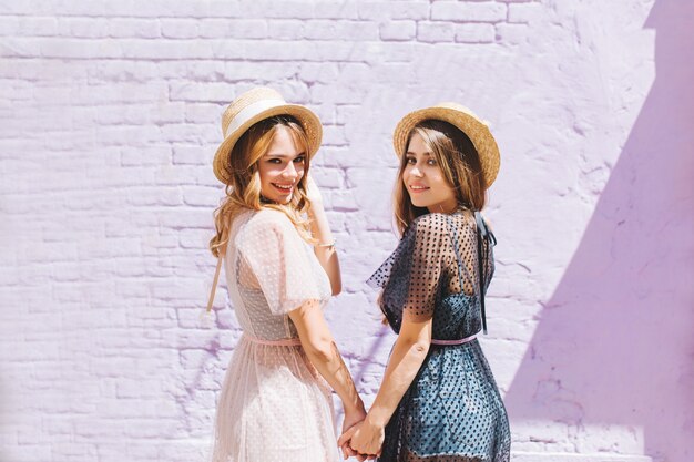 Glad sisters in similar dresses looking over shoulder with inspired smile in sunny day