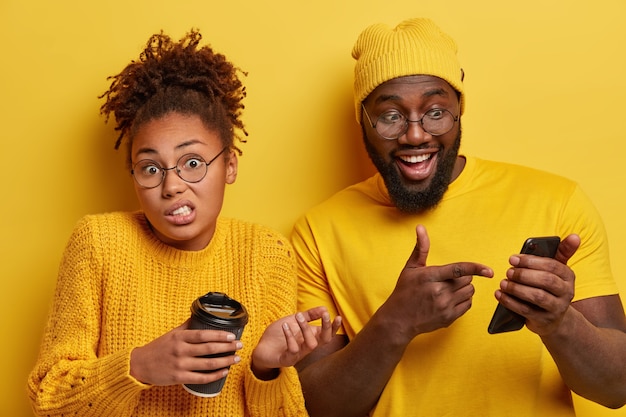 Free photo glad surprised black guy points into screen of smartphone device