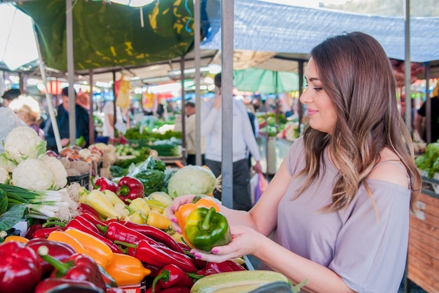 Donna felice scegliendo paprica verde e rossa nel supermercato shoppin