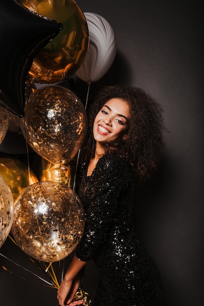 Счастливая женщина с милой улыбкой держит золотые воздушные шары