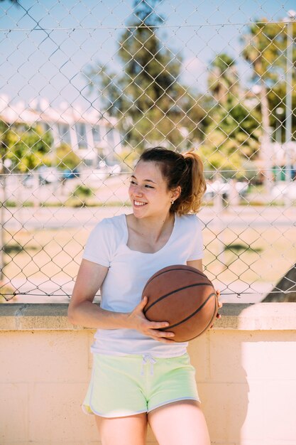 Giovane femmina felice che sta alla rete fissa con pallacanestro