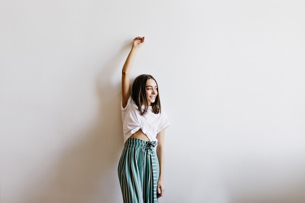 Glad young woman in cute pajamas posing at home. Indoor photo of lovable brunette girl standing.