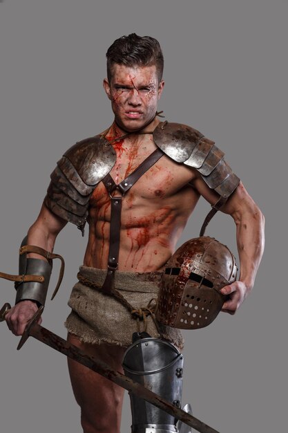 Gladiator with muscular body covered in blood with sword and helmet