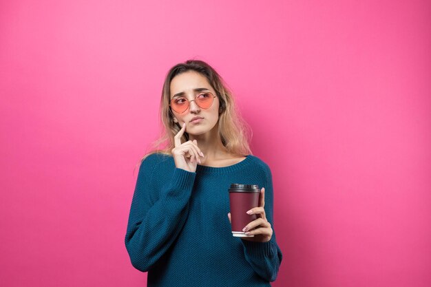ピンク​の​背景​に​コーヒー​を​飲み​ながら​青い​セーター​の​メガネ​の​魅力的​な​女性