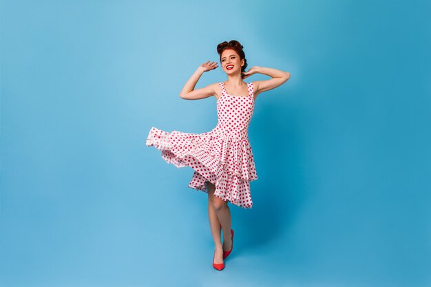 푸른 공간에 춤을 매력적인 생강 소녀. 폴카 도트 드레스에 멋진 핀업 여자의 스튜디오 샷.