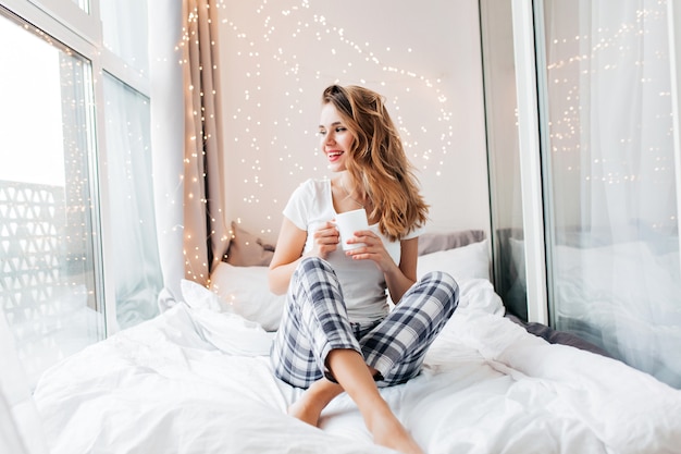 Glamorous girl with happy smile chilling in good morning. Positive female model drinking hot tea.