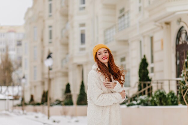 Glamorous long-haired girl posing on blur street. Attractive female model with ginger hair enjoying winter.