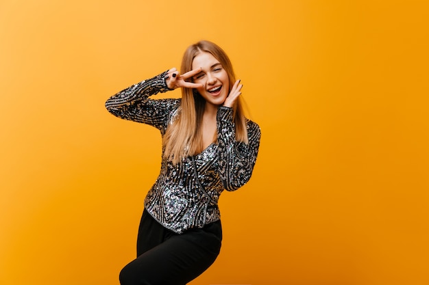 Glamorous white woman with blinde hair funny dancing in studio. Magnificent young woman chilling on orange.