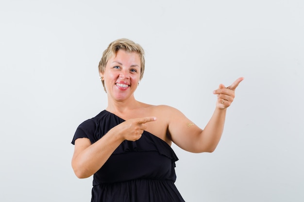 Glamorous woman in black blouse pointing aside 