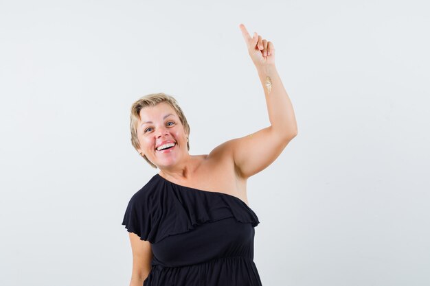 Glamorous woman in black blouse pointing up and looking optimistic 