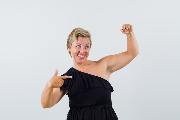 Glamorous woman in black blouse posing like pointing to something at her left hand and looking cheery 