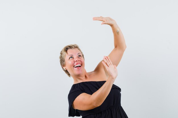 Glamorous woman in black blouse raising hands for defending and looking ready 