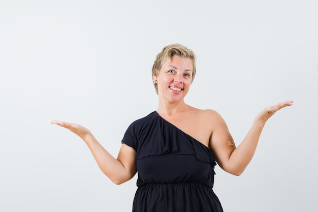 Glamorous woman in black blouse spreading her hands with open palm aside and looking pleased 