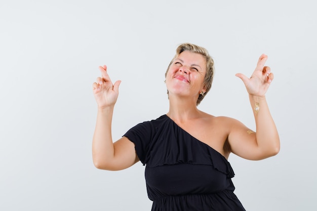 Glamorous woman keeping fingers crossed in black blouse and looking focused 