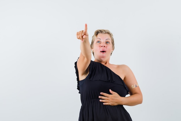 Glamorous woman pointing forward in black blouse and looking astonished 