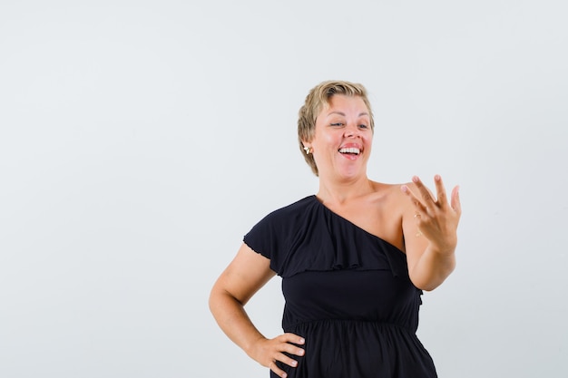 Glamorous woman posing like holding phone in black blouse and looking optimistic 