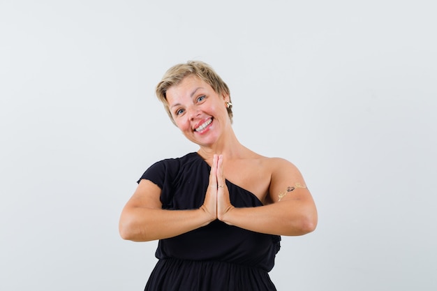 Free photo glamorous woman showing namaste gesture in black blouse and looking pleased