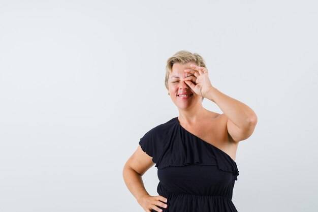 Glamorous woman showing ok gesture on eye in black blouse 