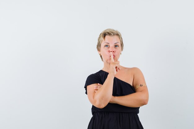 Glamorous woman showing silence gesture in black blouse and looking careful 