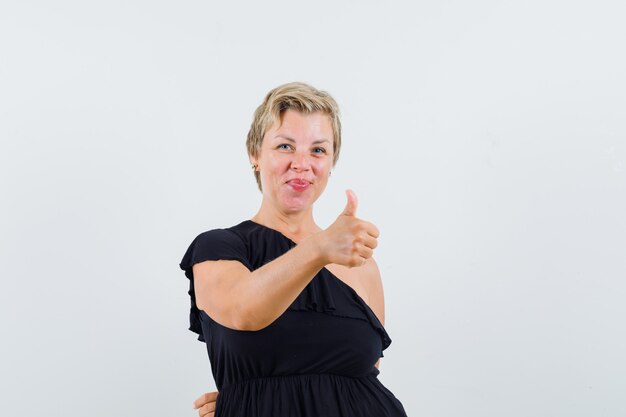 Glamorous woman showing thumb up in black blouse and looking glad. front view.