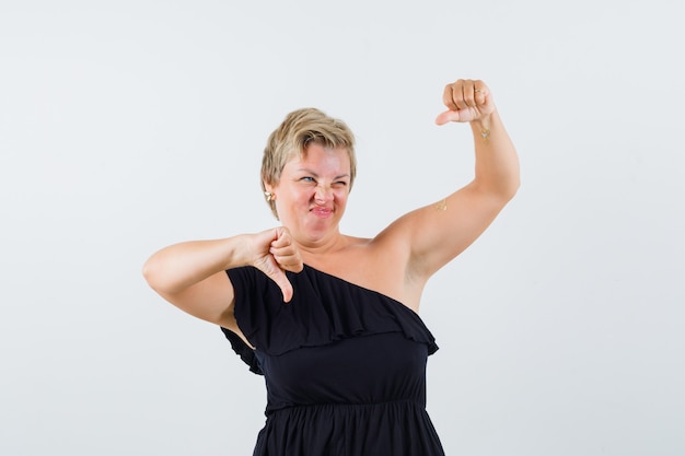 Free photo glamorous woman showing thumb up and down in black blouse and looking hesitant. front view.