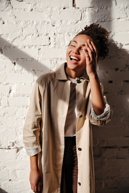 Glamorous woman in trench coat laughing with closed eyes