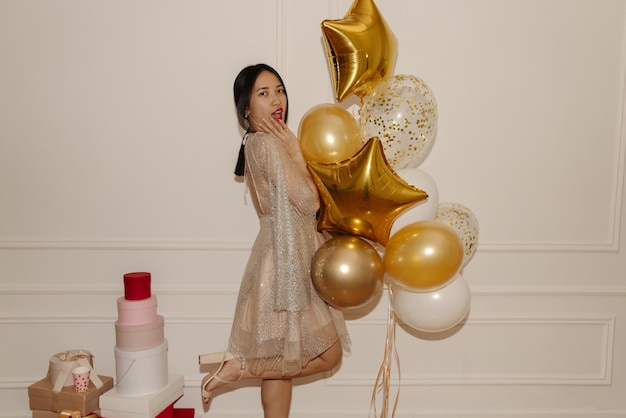 Glamorous young asian brunette lady celebrates birthday with balloons and gifts on white background Concept of enjoying moment