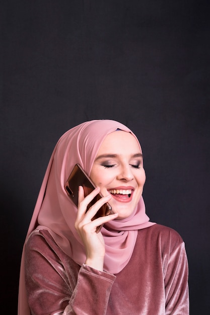 Glamour islamic woman laughing while talking on cellphone in front of black backdrop