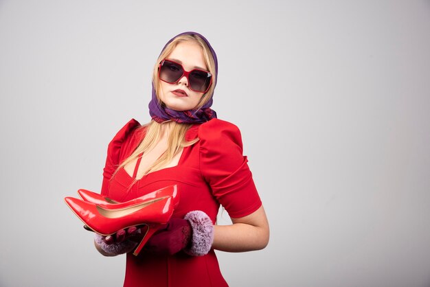 Glamour woman in red outfit posing with pair of heels. 