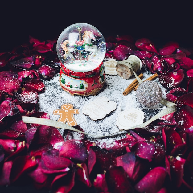 Glass ball with snow and other Christmas decor stands in the circle of red rose petals