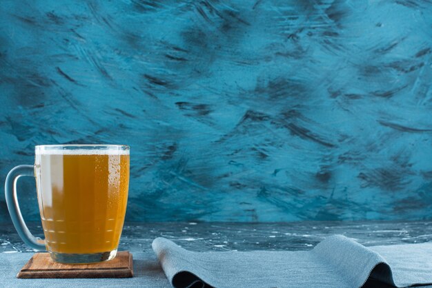 A glass of beer on a board on a pieces of fabric , on the blue table. 