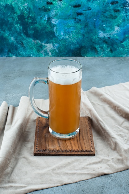 A glass of beer on a board on a towel, on the blue table. 