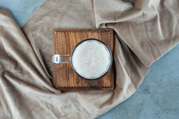 A glass of beer on a board on a towel, on the blue table. 