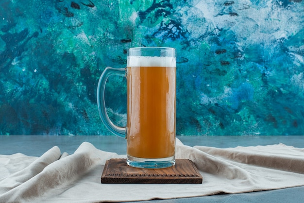 A glass of beer on a board on a towel, on the blue table. 