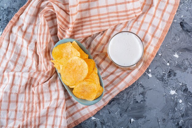 A glass of beer and bowl of chips on tea towel , on the marble surface