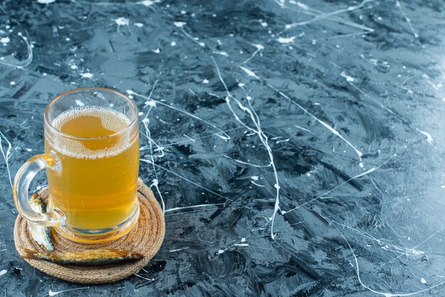 青のトリベットにグラスビールと魚。