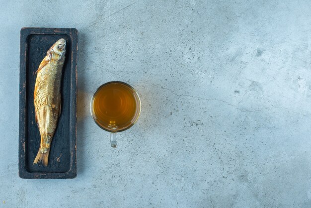 A glass beer of next to fish on a wooden plate, on the blue table. 