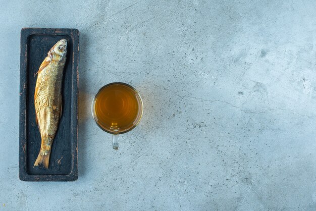 파란색 테이블에 나무 접시에 생선 옆의 유리 맥주.