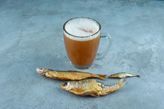 青いテーブルの上にある魚の隣のグラスビール。